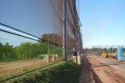 A large mesh fence runs alongside a dirt road with a person standing nearby