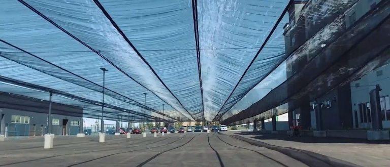 A covered parking area with a translucent blue canopy overhead and cars parked underneath