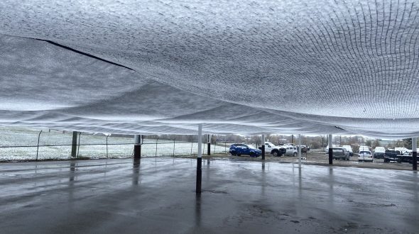 A large canopy structure with vehicles parked underneath on a wet surface