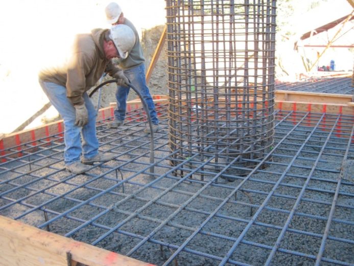 Two construction workers are bending rebar on a reinforced concrete foundation