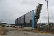 A large industrial structure with a conveyor belt leans against a building