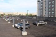 Parking lot with cars and wind fence posts near a multi-story building