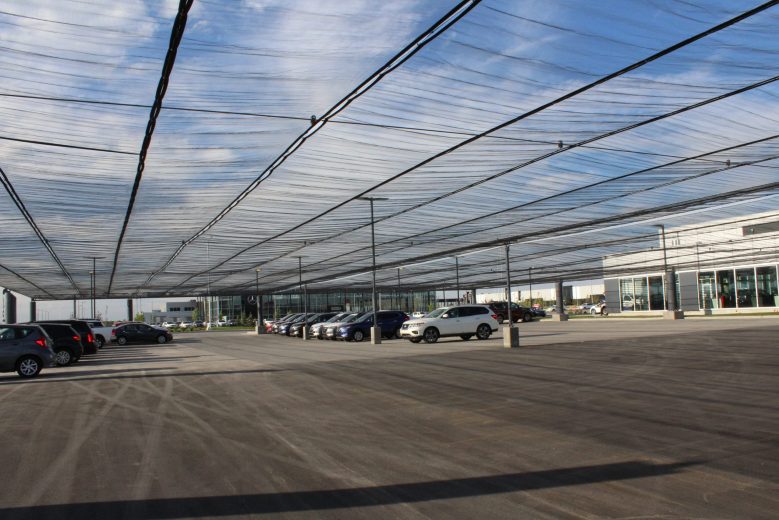 A large parking lot with cars parked under a mesh canopy structure