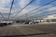 A large parking lot with cars parked under a mesh canopy structure