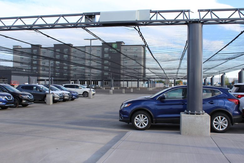 A parking lot with a black mesh canopy covering rows of parked cars