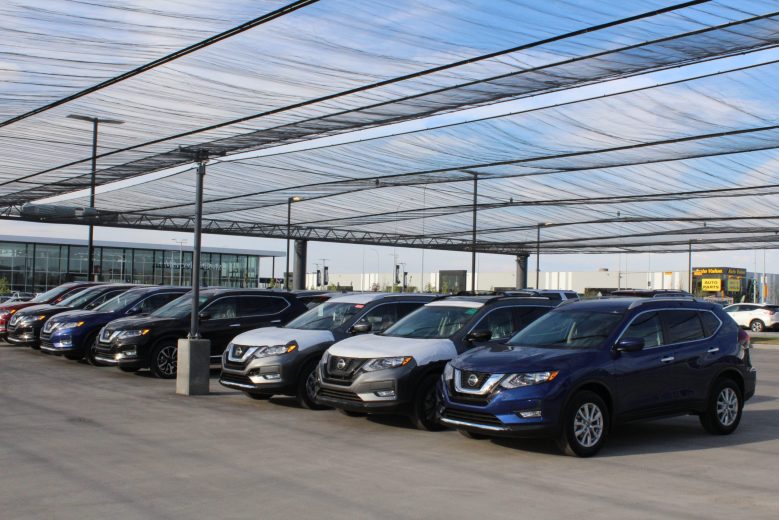 Several cars parked under a large, translucent canopy at a dealership