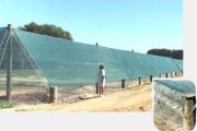 A person stands next to a long green wind fence supported by wooden posts