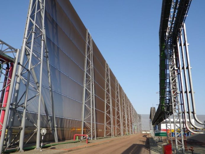 Large industrial wind fence with metal framework and adjacent conveyor system