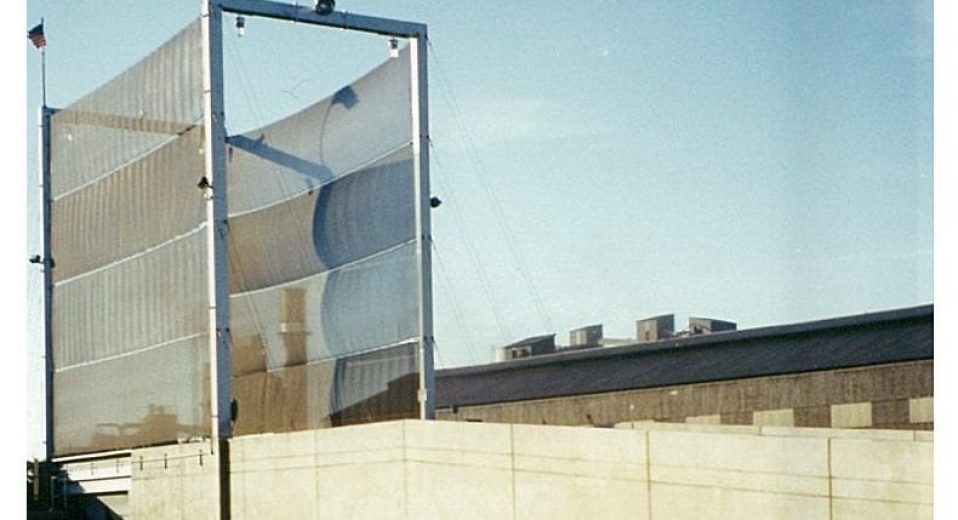 A tall, metal-framed wind fence with fabric panels stands against a clear sky