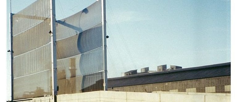 A tall, metal-framed wind fence with fabric panels stands against a clear sky
