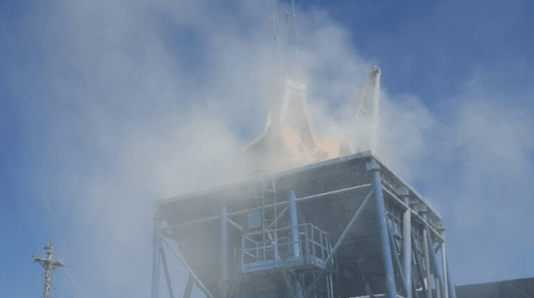 A metal structure emits smoke against a clear blue sky