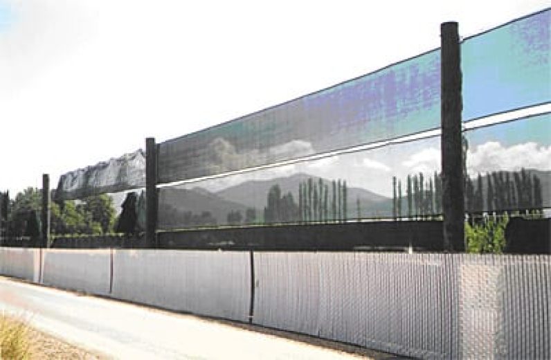 A tall, dark mesh fence stretches across a landscape with mountains in the background