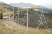 A large gravel pile is covered by a wind fence supported by metal poles