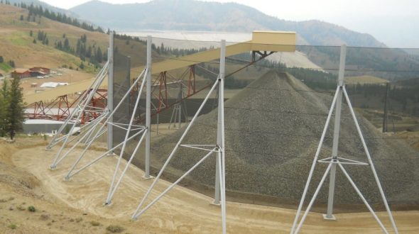 A large gravel pile is covered by a wind fence supported by metal poles