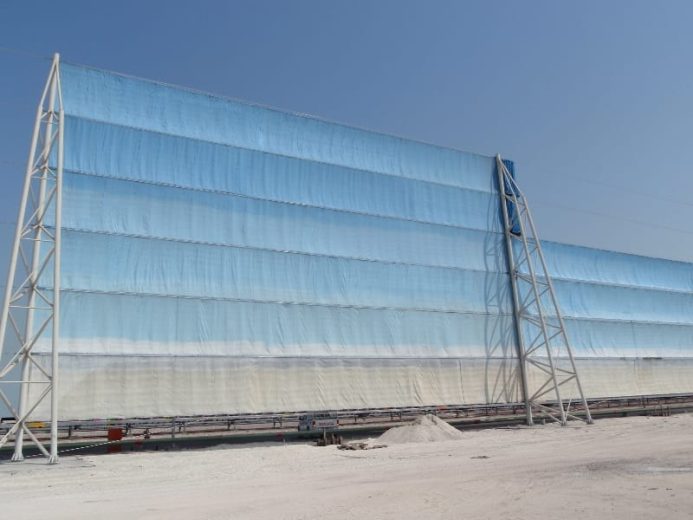 A large blue and white wind fence structure stands against a clear sky