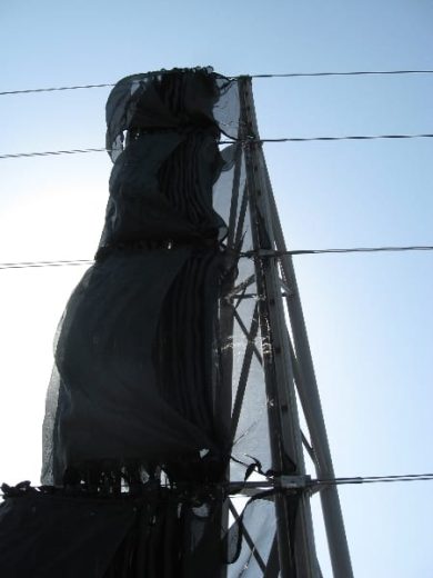 A black mesh wind fence attached to a tall metal frame against a clear sky