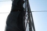 A black mesh wind fence attached to a tall metal frame against a clear sky