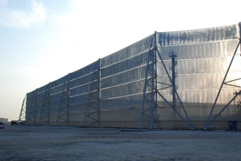 A large industrial wind fence stretches across a flat, dusty area