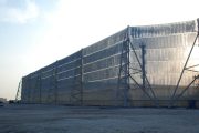 A large industrial wind fence stretches across a flat, dusty area