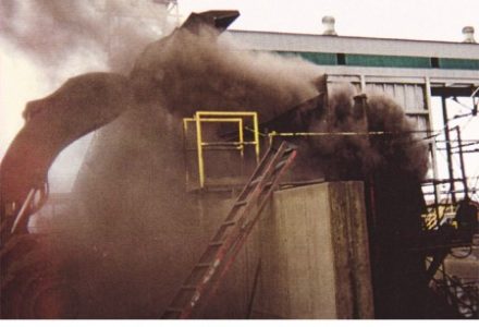 A large industrial machine emits thick black smoke without any dust control measures in place