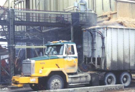 A yellow and white truck is parked next to a large industrial building