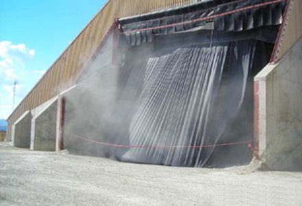 A large industrial building with dust control curtains and a gravel ground