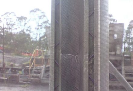 A gloved hand touches a section of industrial fencing or netting outdoors