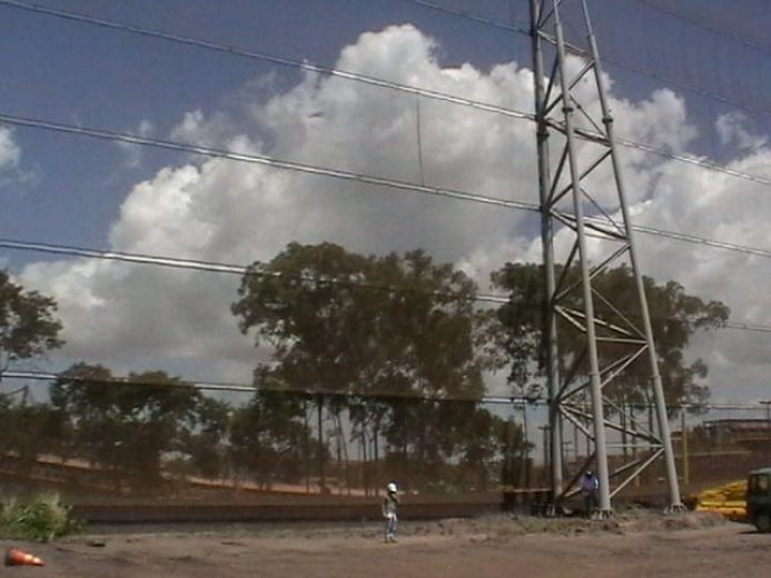 A large metal windbreak structure stands against a backdrop of trees and clouds
