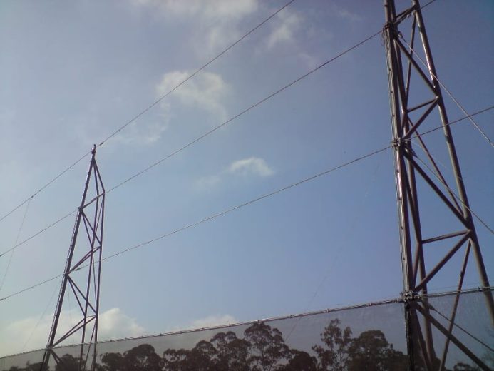 Two tall metal towers with cables against a clear sky and trees in the background