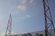 Two tall metal towers with cables against a clear sky and trees in the background