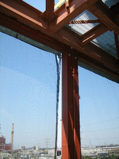 A metal structure with a mesh screen overlooking an industrial area with smokestacks