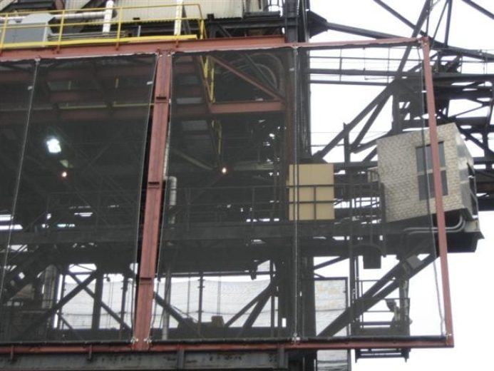 Industrial structure with metal framework and mesh panels, featuring yellow railings and lighting
