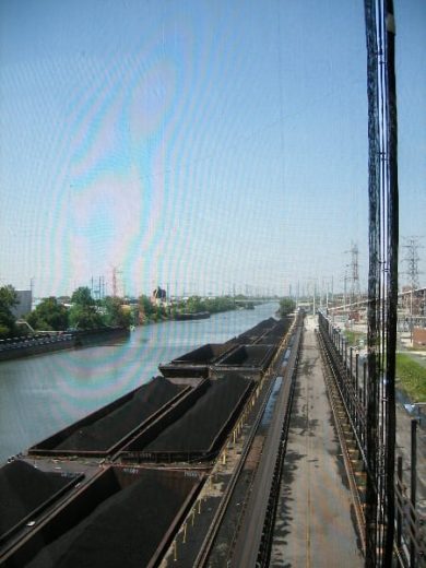 Coal barges on a river beside a road and power lines under a clear sky
