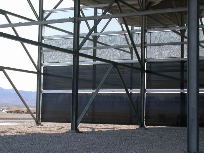 A large metal framework structure with dark panels and a gravel ground