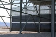 A large metal framework structure with dark panels and a gravel ground