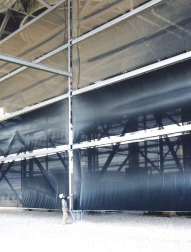 A person stands next to a large industrial wind fence or dust control structure