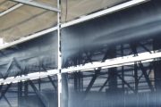 A person stands next to a large industrial wind fence or dust control structure