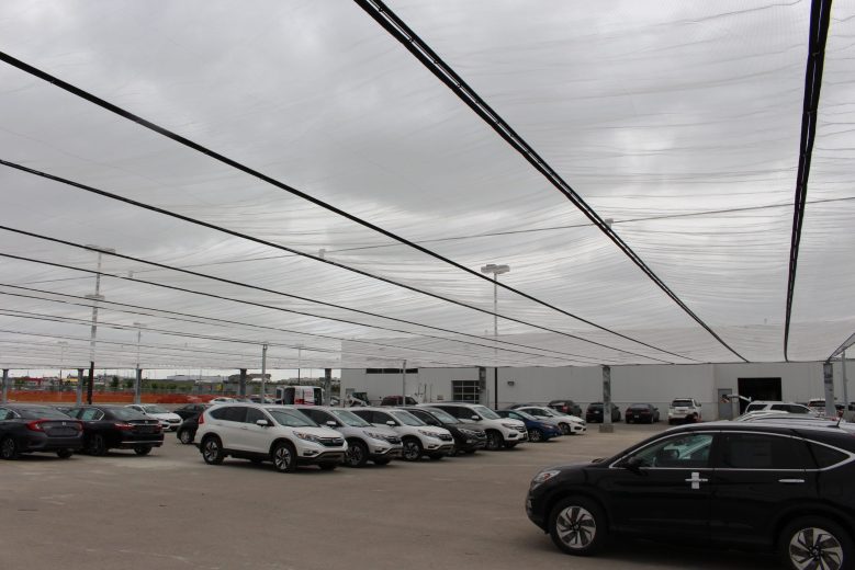 Cars parked under a large translucent canopy on a cloudy day