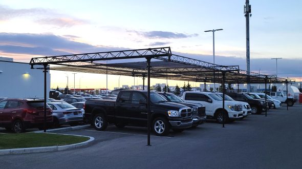 A parking lot with vehicles parked under a metal canopy structure at sunset