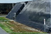 Large black mesh wind fence installed on a grassy slope near a paved path