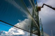 A large green metal structure with a translucent covering against a backdrop of clouds and a rainbow