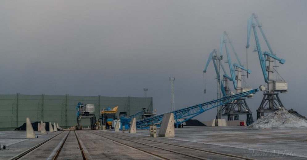 Industrial cranes and conveyor belts on a concrete dock with piles of material