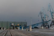 Industrial cranes and conveyor belts on a concrete dock with piles of material