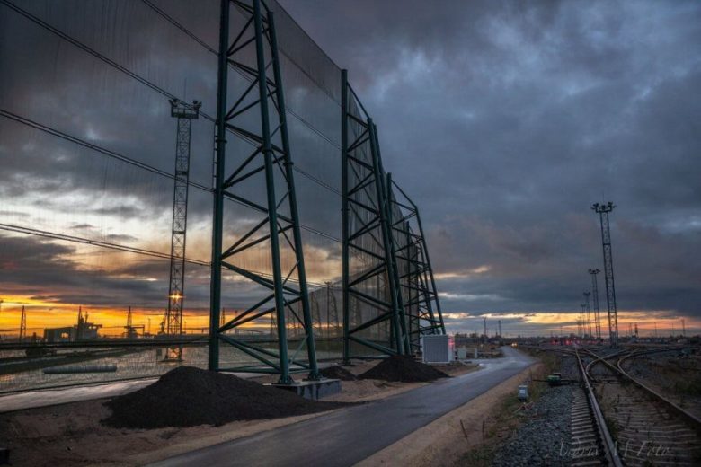 A large industrial wind fence stands against a dramatic sunset sky