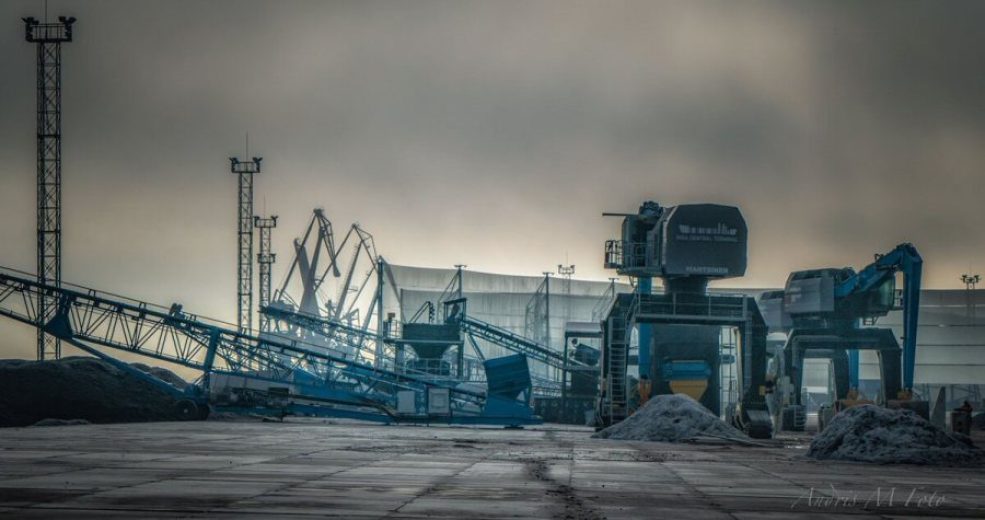 Industrial site with conveyor belts, cranes, and piles of material under a cloudy sky
