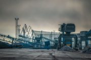 Industrial site with conveyor belts, cranes, and piles of material under a cloudy sky