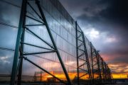 A large industrial wind fence stands against a dramatic sunset sky