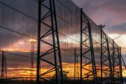 A large industrial fence structure stands against a vibrant sunset sky