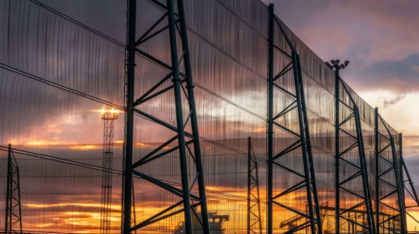 A large industrial fence structure with a sunset visible through the mesh