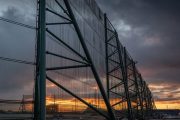 A large industrial fence structure with a sunset visible through its mesh panels